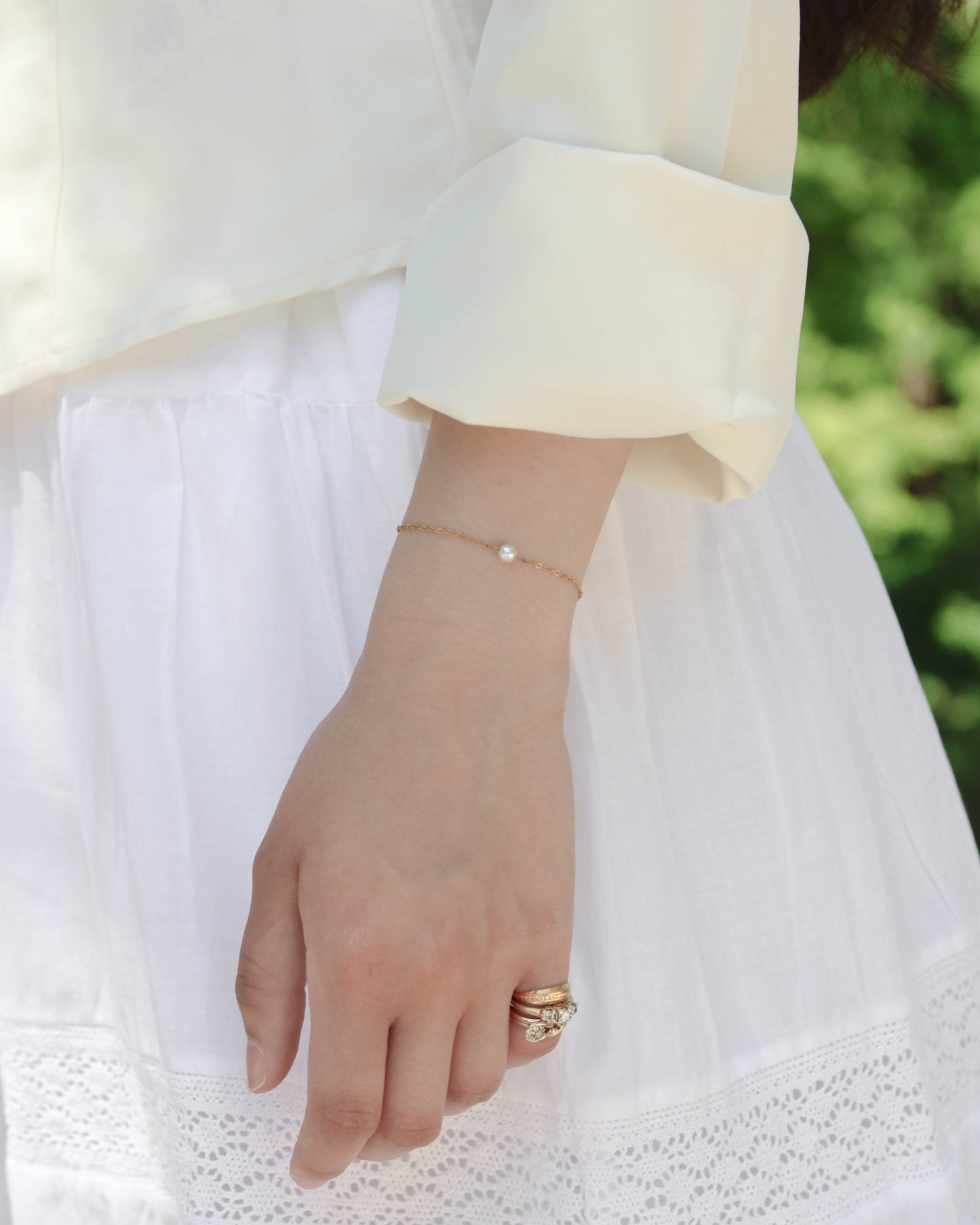 Single pearl bracelet on wrist on a girl with a white outfit outside