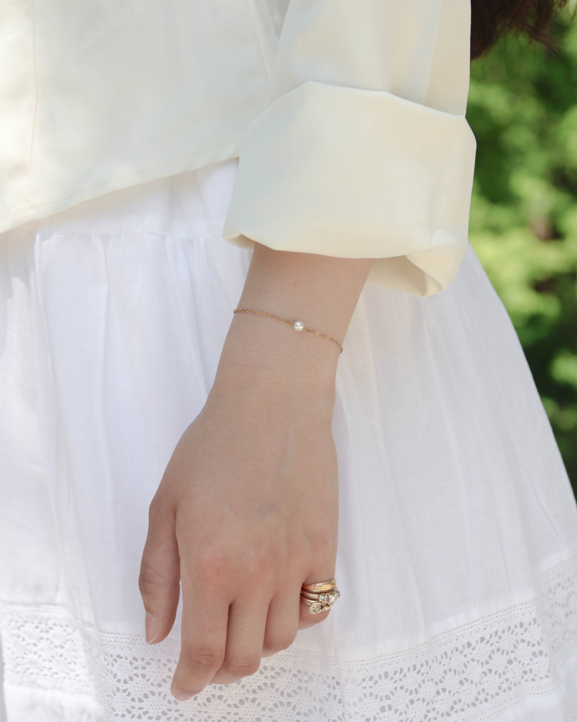 Single pearl bracelet on wrist on a girl with a white outfit outside