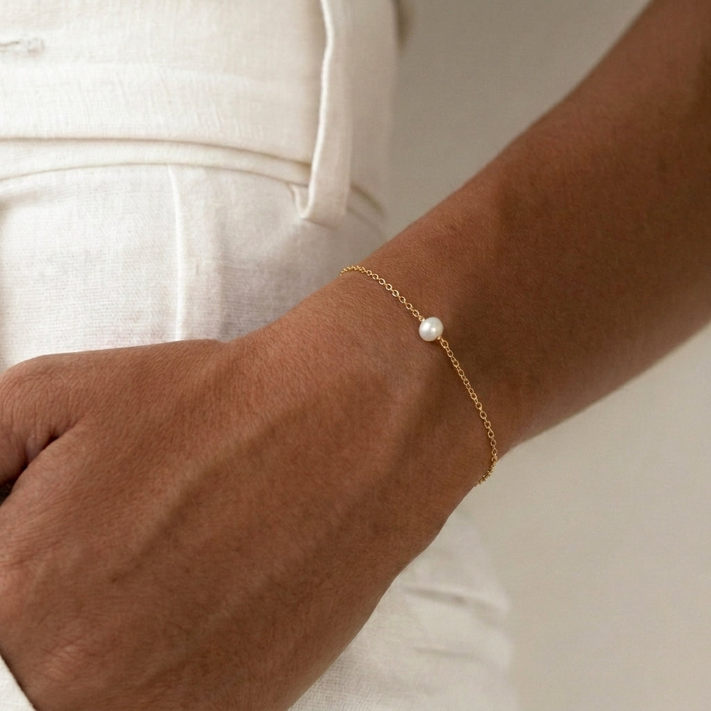 Gold bracelet with a pearl on a wrist with hand in pockets